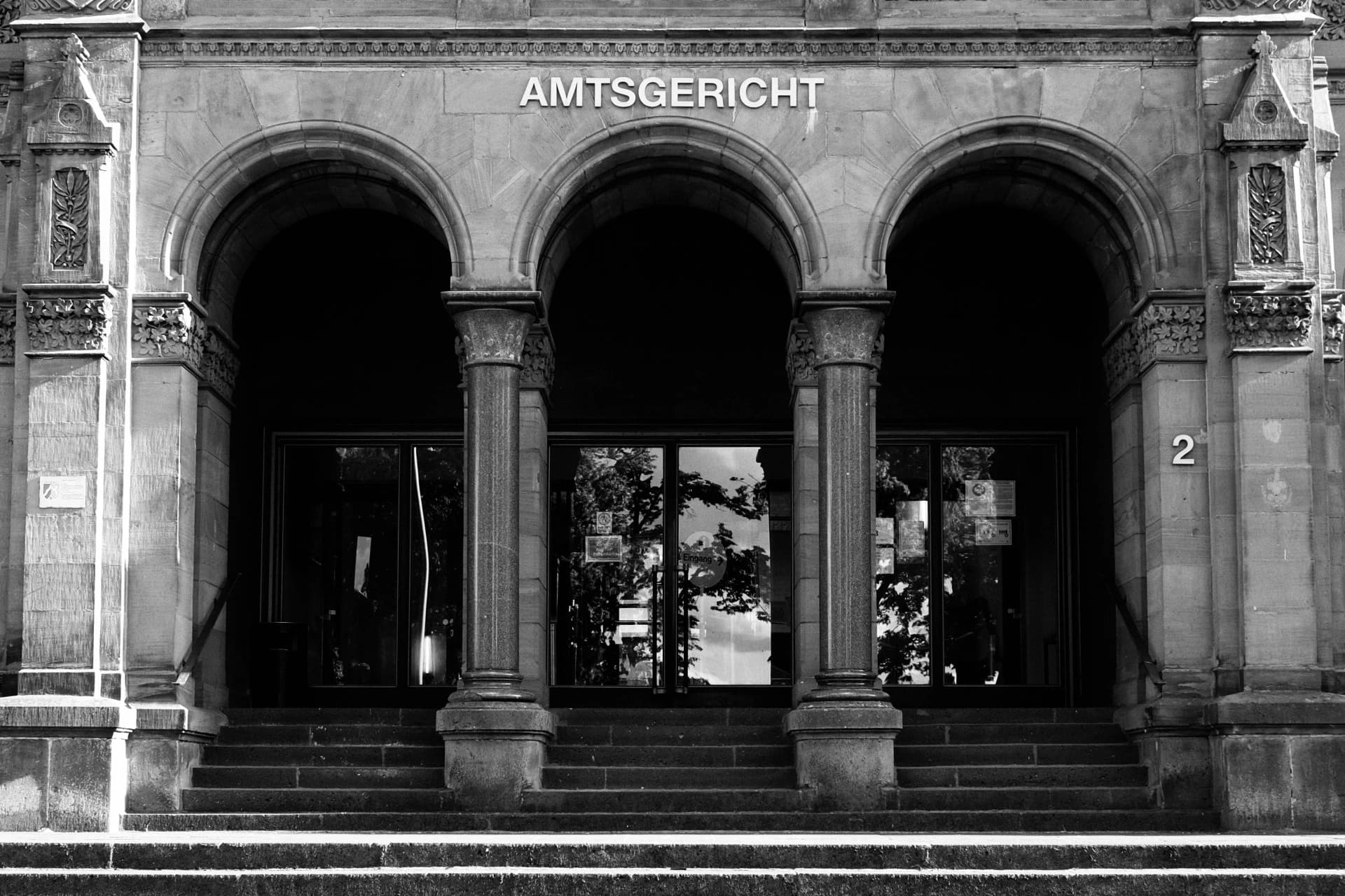 Sandsteinfassade mit der Aufschrift „Amtsgericht“ über einer dreibögigen Eingangsarkade mit Säulen und Glastüren.
