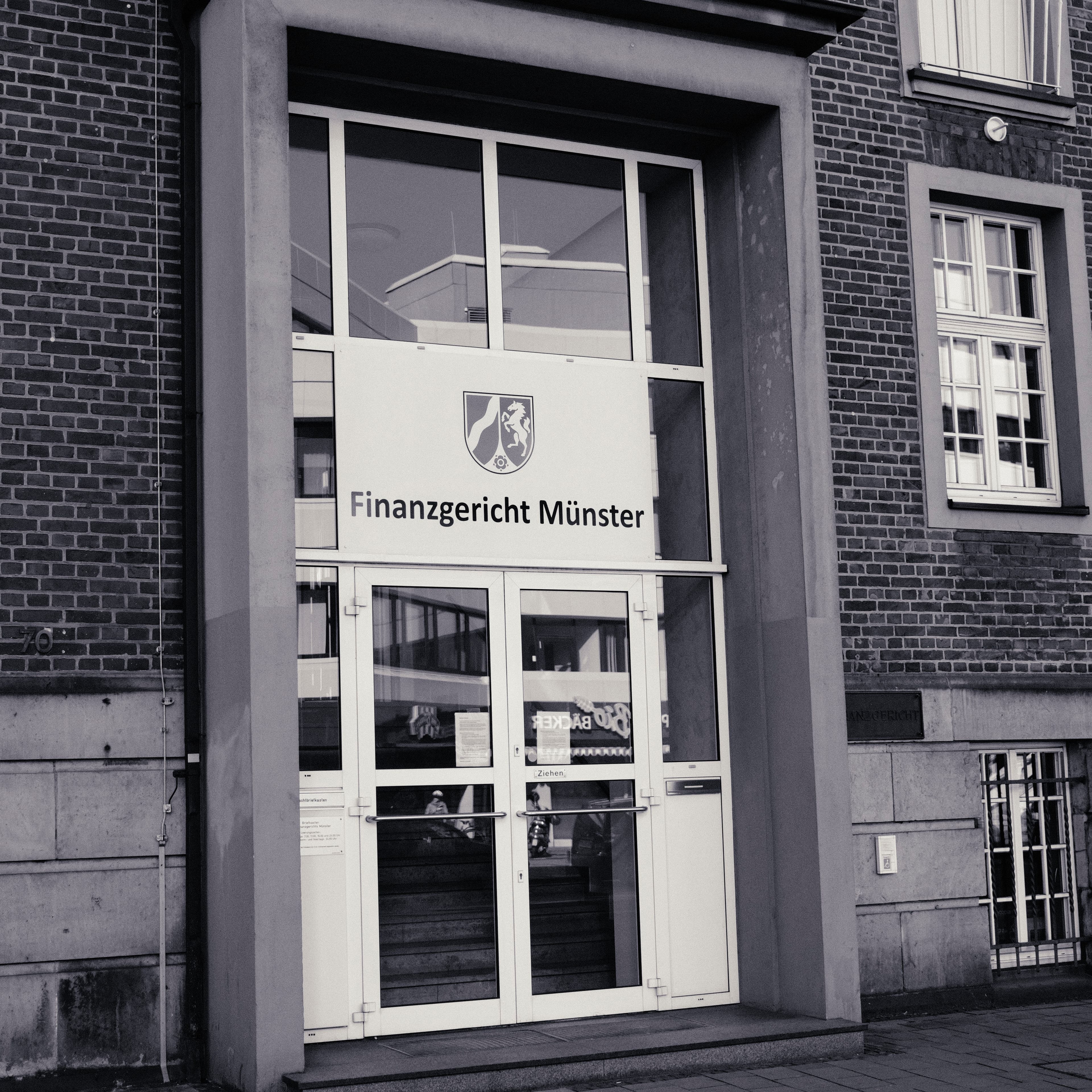 Eingangsportal des Finanzgerichts Münster mit Landeswappen Nordrhein-Westfalen und Beschriftung über der Glastür.
