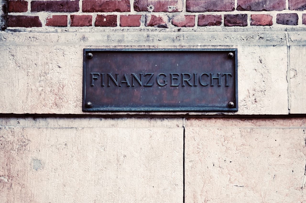 Verwitterte Bronzetafel mit der Aufschrift „Finanzgericht“ an einer Sandstein- und Ziegelfassade.